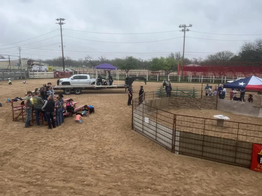 The Ham Rodeo arena at Mansfield Park before the hog catch: the catch pen, a flatbed stage, the Texas-flag tent and the red bleachers.