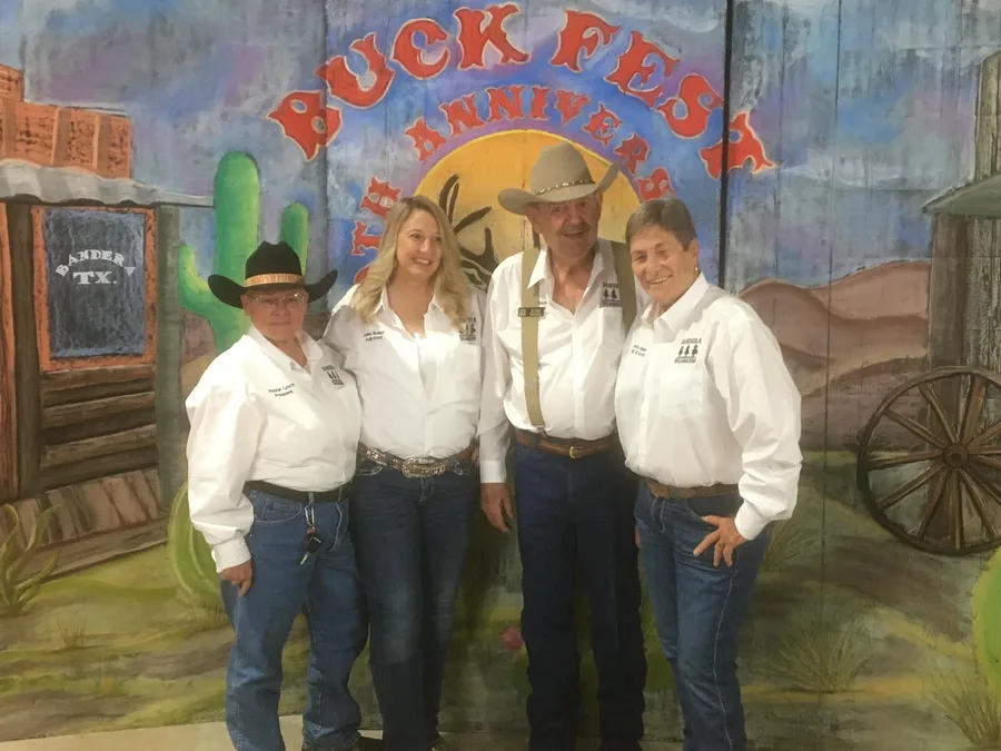 Wranglers members in white club shirts and cowboy hats in front of the painted Buck Fest backdrop.