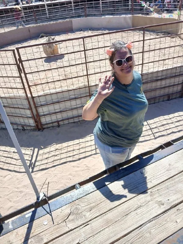 A smiling Wrangler in pig-ear headband waves from the arena fence at the Ham Rodeo.