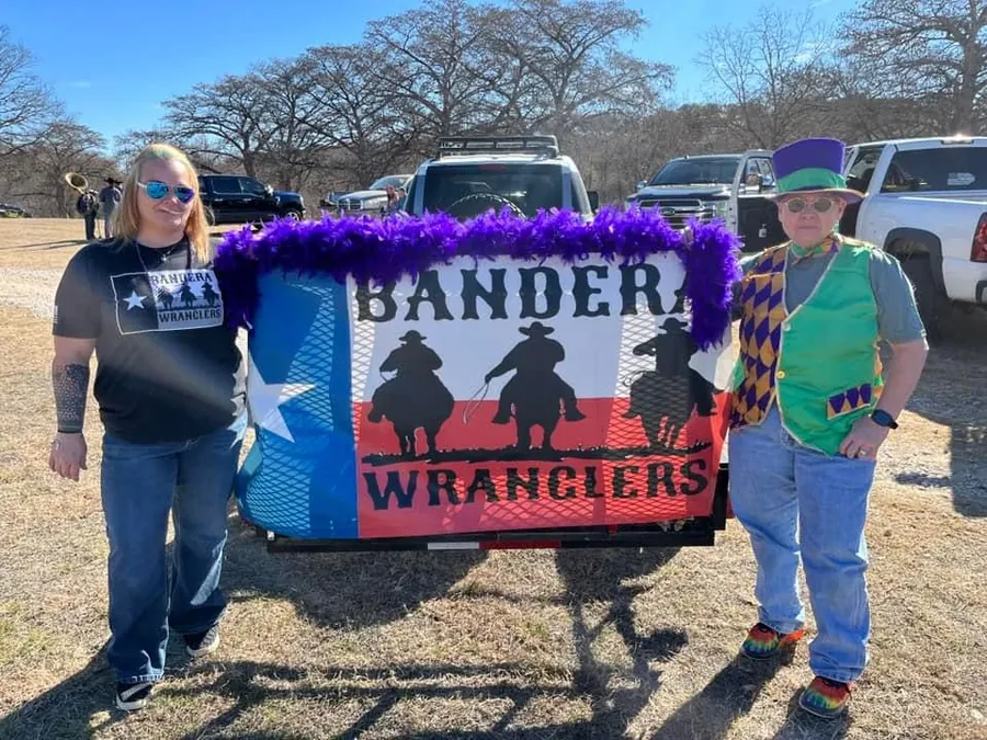 Two Bandera Wranglers in parade costumes beside the Bandera Wranglers Texas-flag banner.